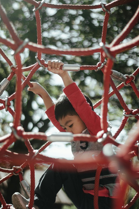 A child playing on a red metal playground climbing frame